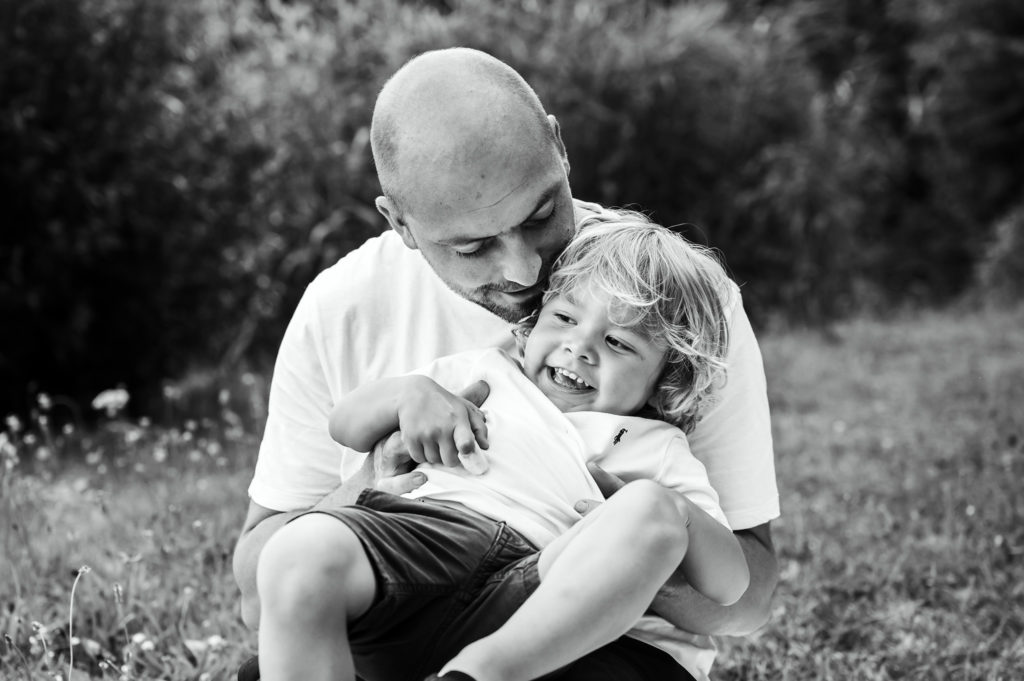 Speelse zwart-wit foto van vader en zoon tijdens een gezinsfotoshoot in een stuk natuur te Zwevegem